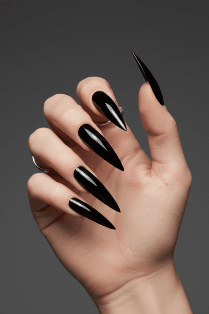 Detailed close-up of a fierce stiletto nail shape with a black chrome metallic finish, focusing on the sharp needle-point tip and precision filing work