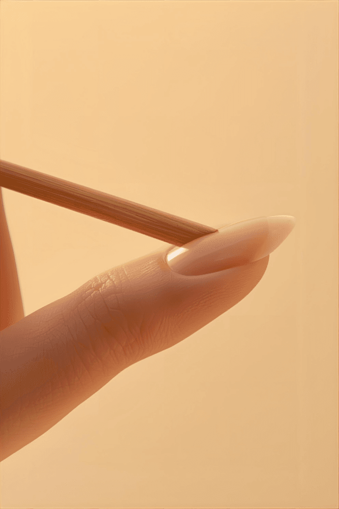 Close-up of a woman gently pushing back her cuticles with a wooden orange stick to prepare for a DIY manicure