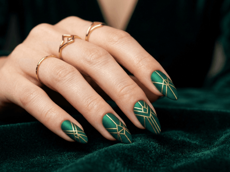 A finished professional geometric nail design with sharp black and gold lines on a matte base.